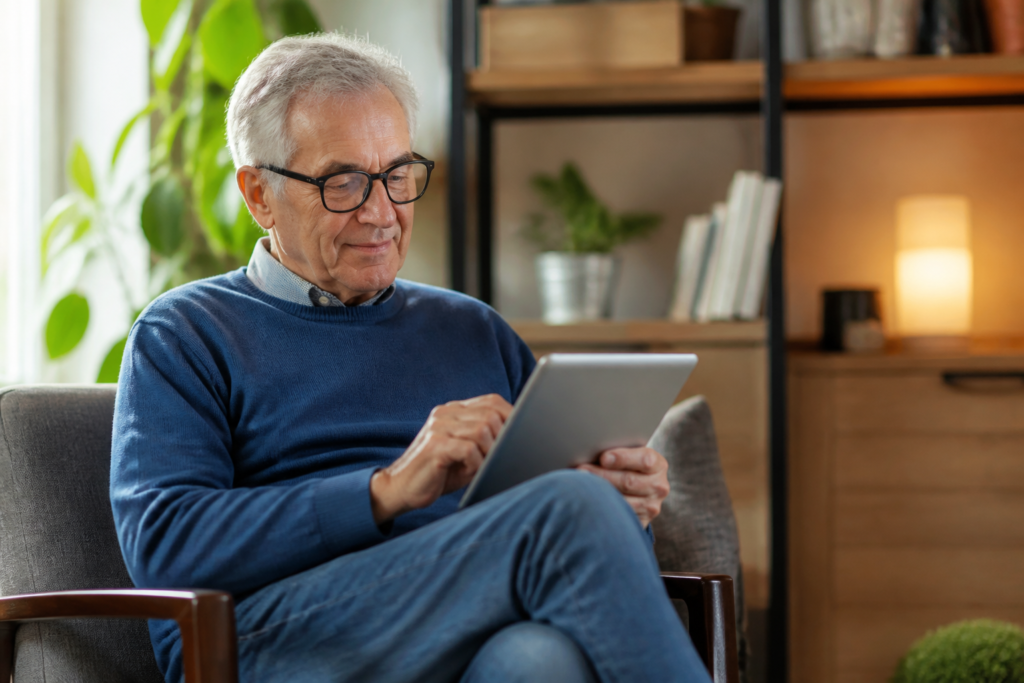 A senior man typing an email on a tablet in a cozy corner of his home