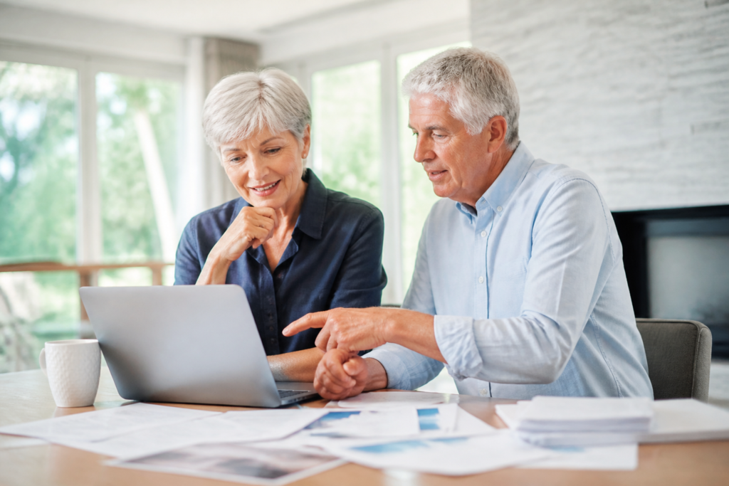 A senior couple using a laptop with papers spread around them, discussing their online business prospects